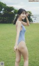 A woman in a blue one piece swimsuit standing in the grass.