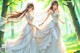 A couple of women in wedding dresses walking through a forest.