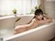 A naked woman sitting in a bathtub with a plant in the background.