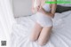 A woman in a white bodysuit sitting on a bed.