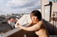 A naked woman standing on a balcony with a city in the background.