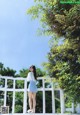 A woman standing on a white fence in front of a tree.