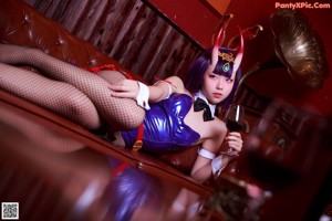 A woman in a blue dress sitting on a couch holding a glass of wine.