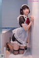 A woman in a maid outfit leaning against a wall.